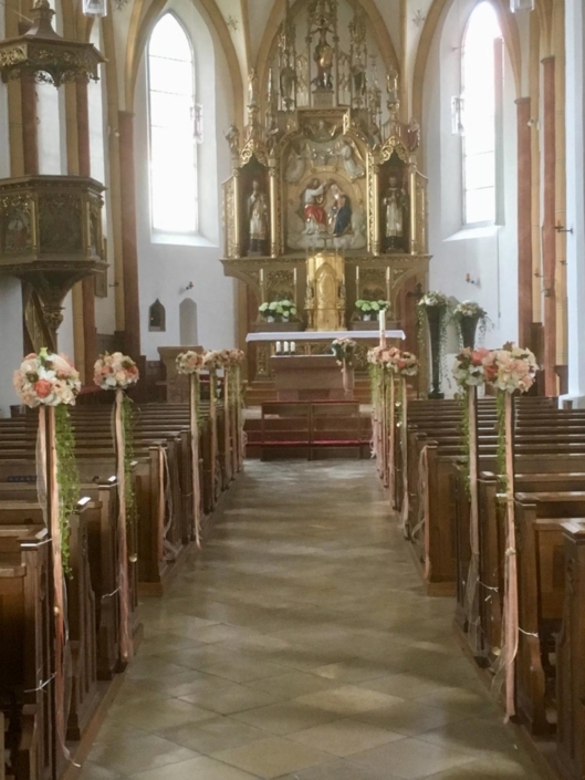 Mit Blumensträußen dekorierte Kirchenbänke für eine Hochzeitsfeier.